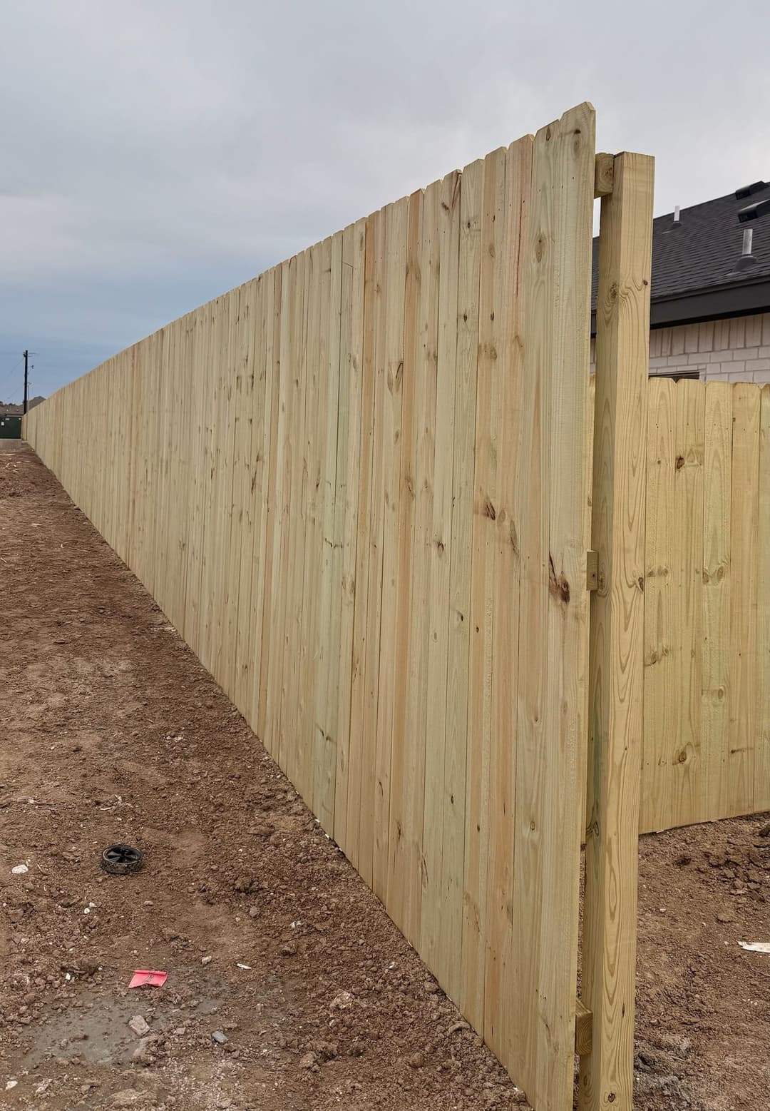 New wooden fence panel under construction on a cloudy day, with dirt ground visible.