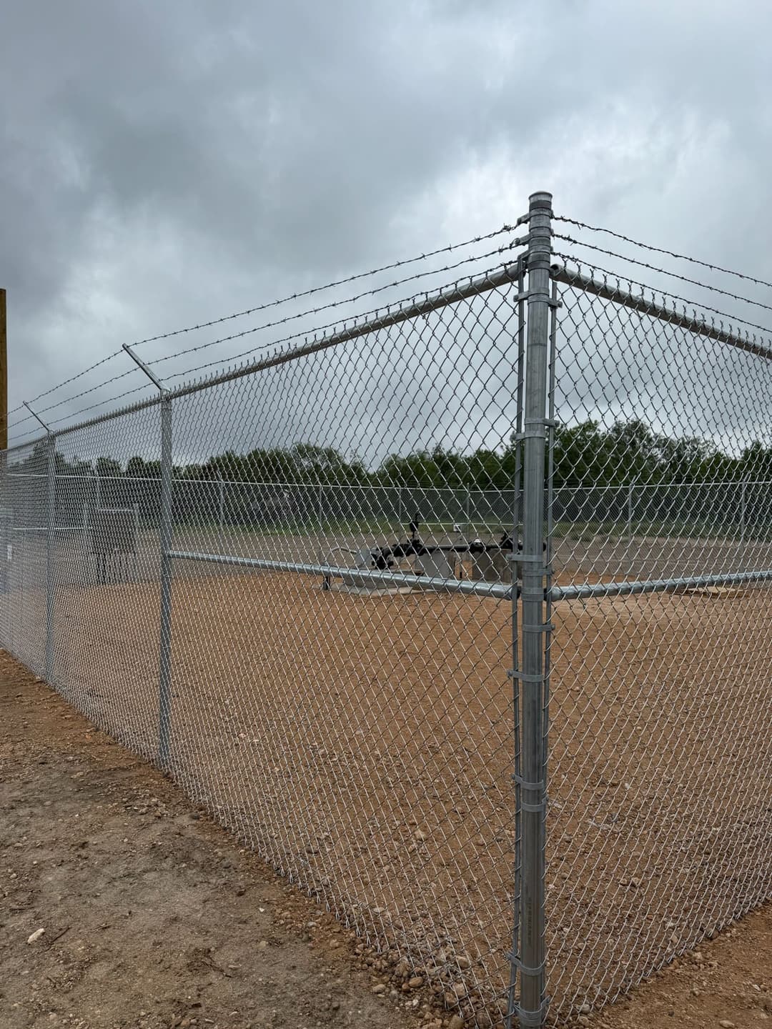 Chain-link fenced baseball field with cloudy skies in the background.