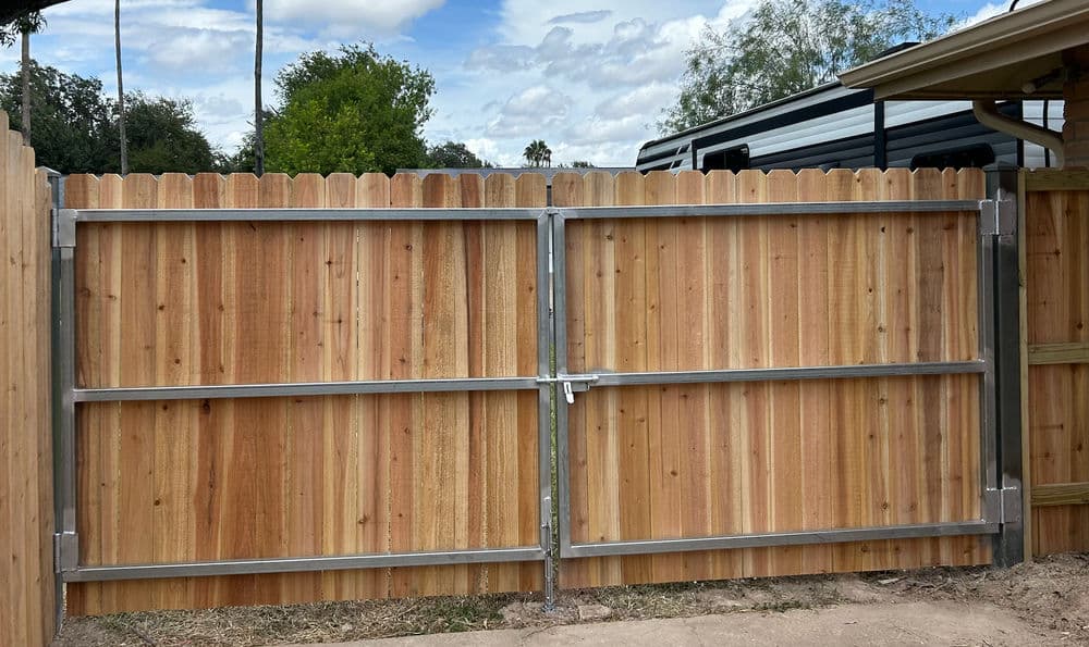 Wooden fence gate with metal hardware, set in a residential backyard surrounded by greenery.