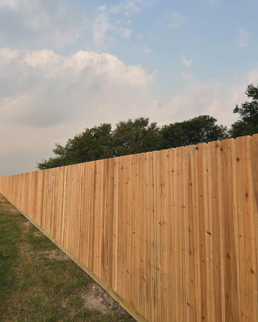 Wooden fence stretching along a grassy area under a cloudy sky.