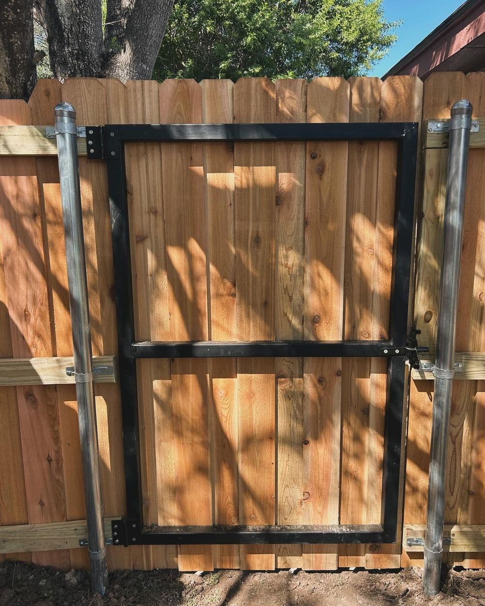Metal fence gate mounted on a wooden fence with a natural wood finish.