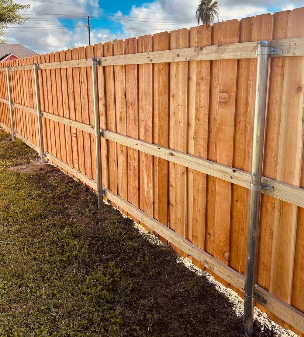 Wooden fence with metal supports under a blue sky, surrounded by green grass.