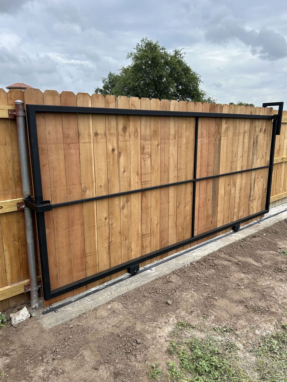 Modern wooden sliding gate with metal frame installed in a rural landscape.
