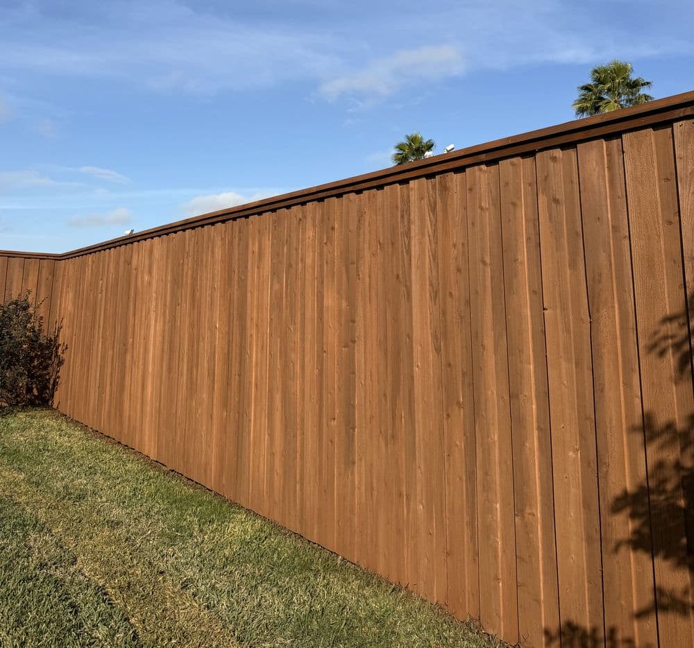 Wooden fence extending into the distance with blue sky and palm trees in the background.