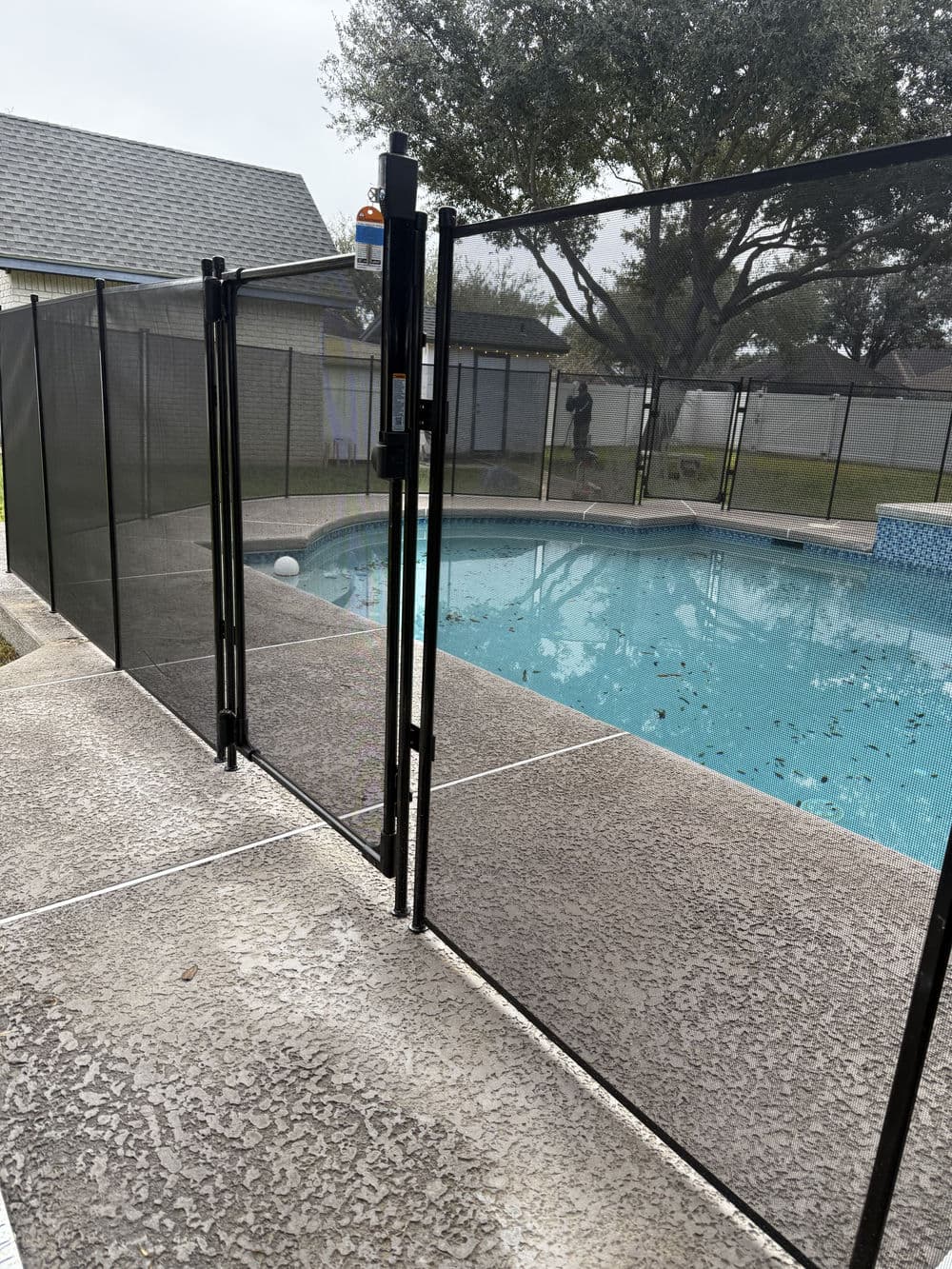 Safety pool fence surrounding a swimming pool with trees in the background.