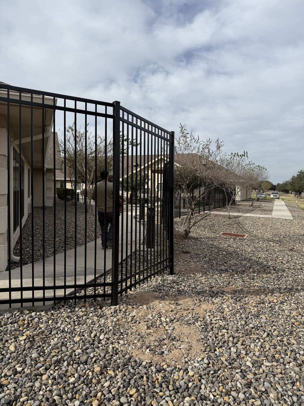 Black metal gate leading to a walkway in a residential area with gravel landscaping.