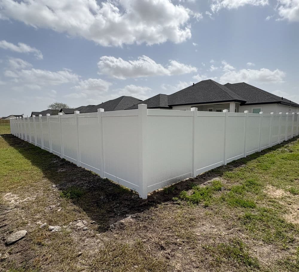 White vinyl fence enclosing a yard with homes visible in the background under a cloudy sky.