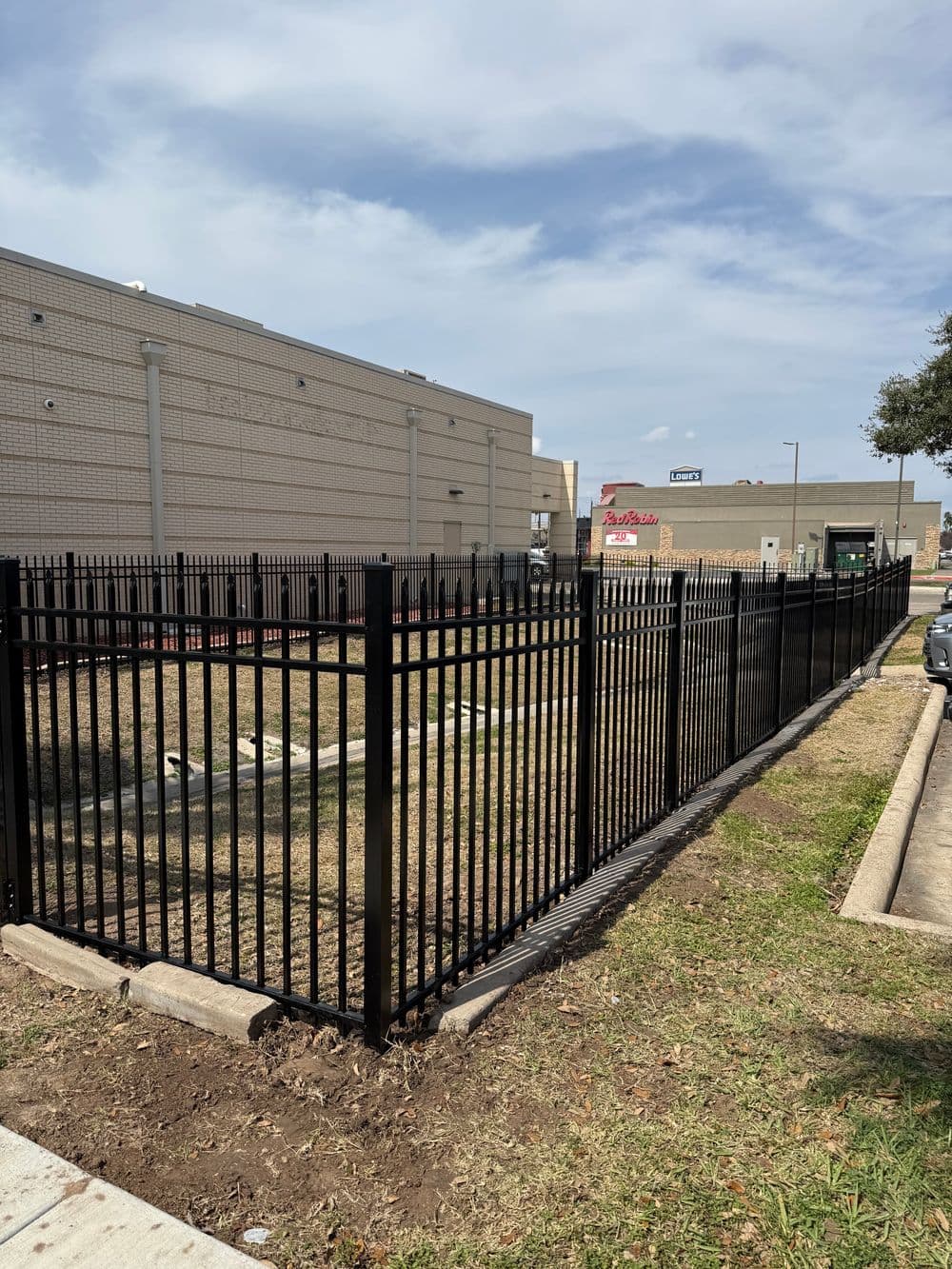 Black metal fence surrounding an empty lot next to a commercial building.