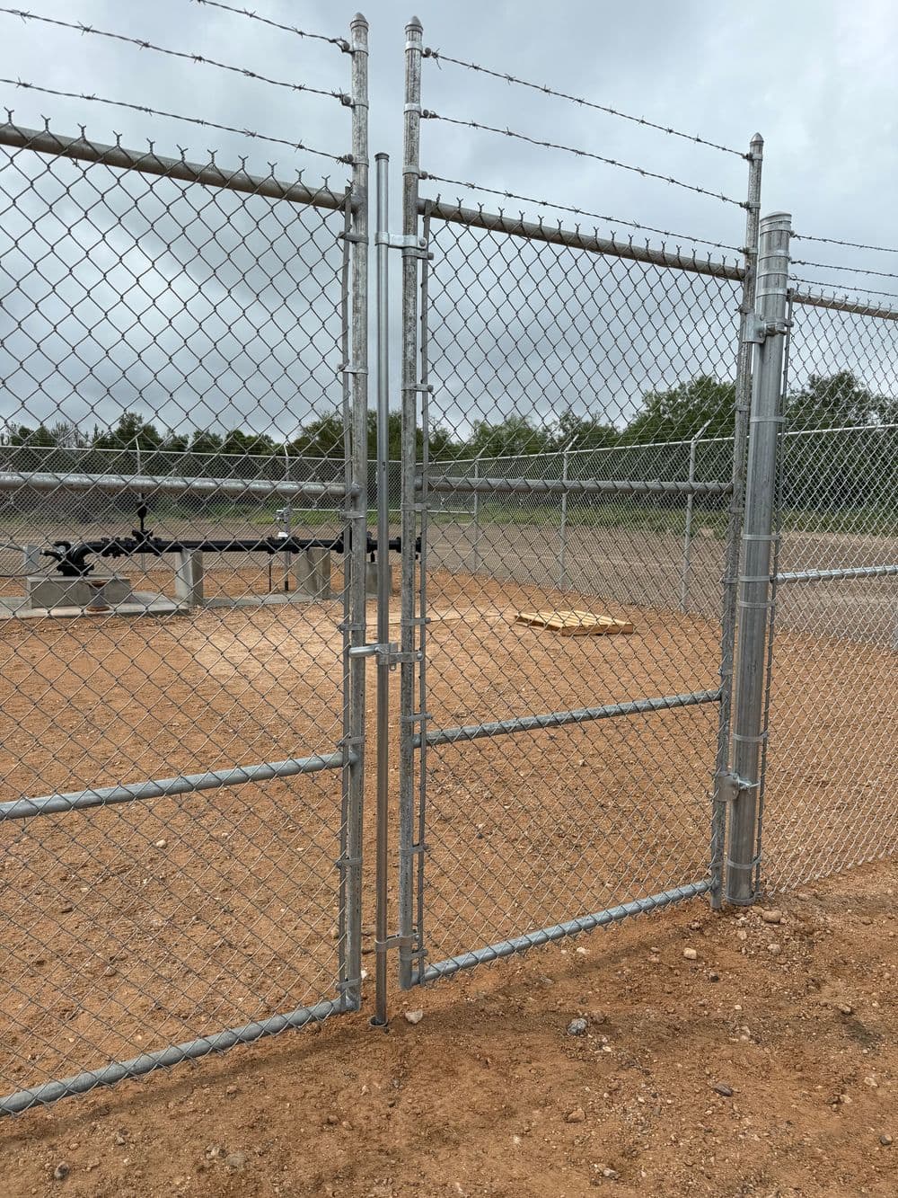 Chain link fence gate opening to a sandy area, suitable for outdoor activities or a dog park.